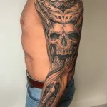 Tatouage noir et gris cicatrisé sur bras complet, représentant un crâne, un hibou et des rouages – Jake Tattoo Parlor à Belfort.