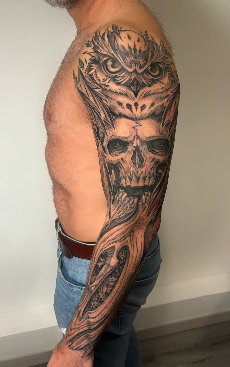 Tatouage noir et gris cicatrisé sur bras complet, représentant un crâne, un hibou et des rouages – Jake Tattoo Parlor à Belfort.
