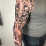 Tatouage noir et gris sur un bras complet représentant des crânes et des ornements de style cathédrale – Jake Tattoo Parlor à Belfort.