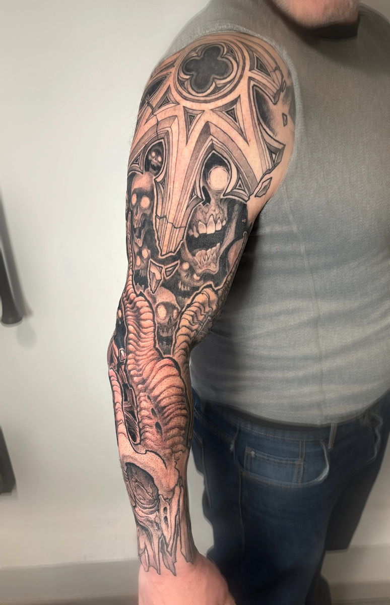 Tatouage noir et gris sur un bras complet représentant des crânes et des ornements de style cathédrale – Jake Tattoo Parlor à Belfort.