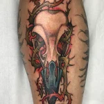 Tatouage néo-trad couleur représentant un crâne de corbeau sur le tibia – Jake Tattoo Parlor à Belfort.