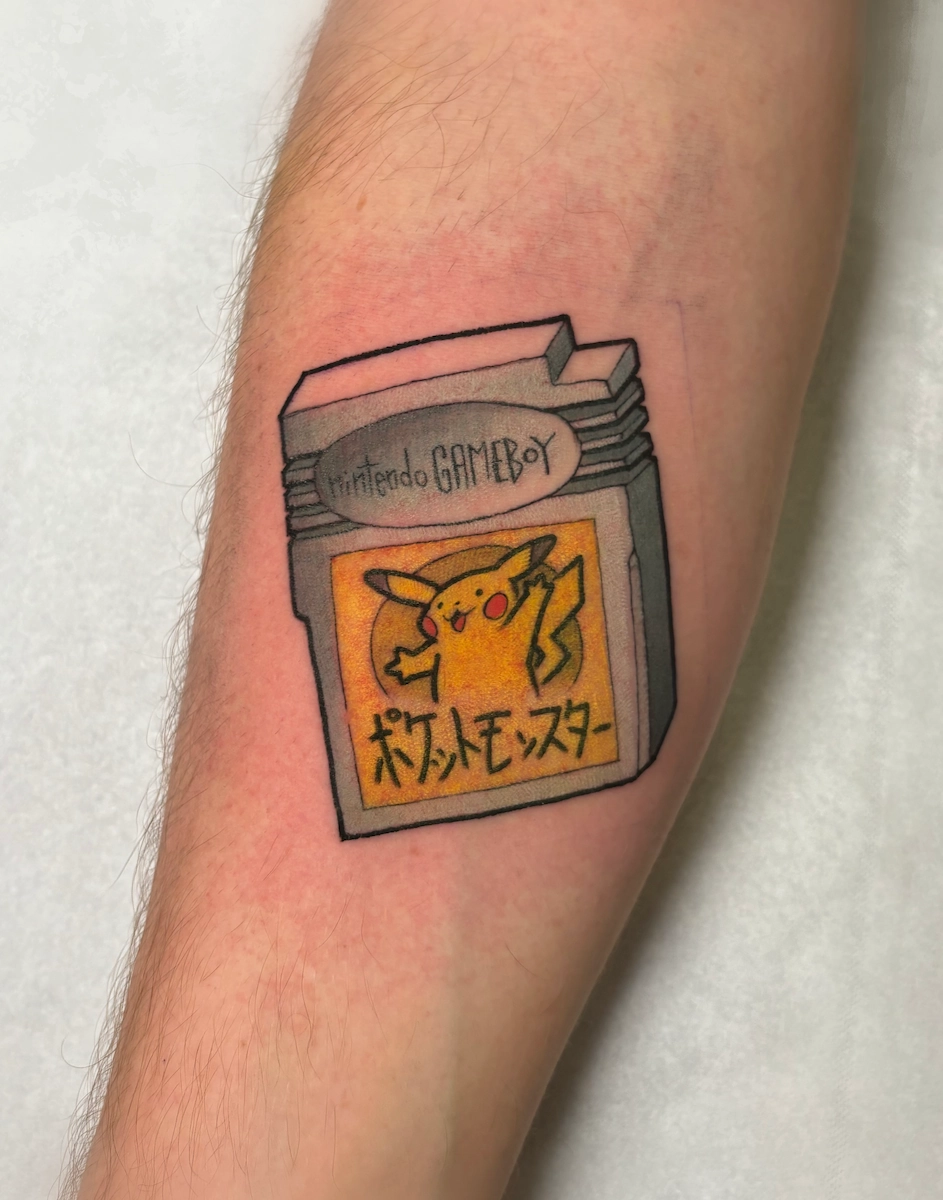 Tatouage couleur sur l’avant-bras représentant une cartouche Game Boy Pokémon Jaune – Jake Tattoo Parlor à Belfort.