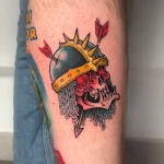Tatouage néo-trad couleur représentant une tête de mort portant un casque de chevalier transpercée par des flèches – Jake Tattoo Parlor à Belfort.