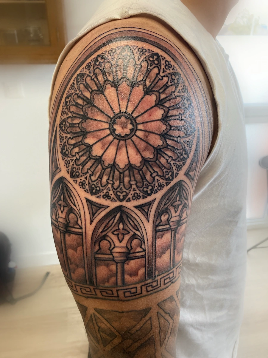 Tatouage ornemental noir et gris représentant une rosace de cathédrale – Jake Tattoo Parlor à Belfort.
