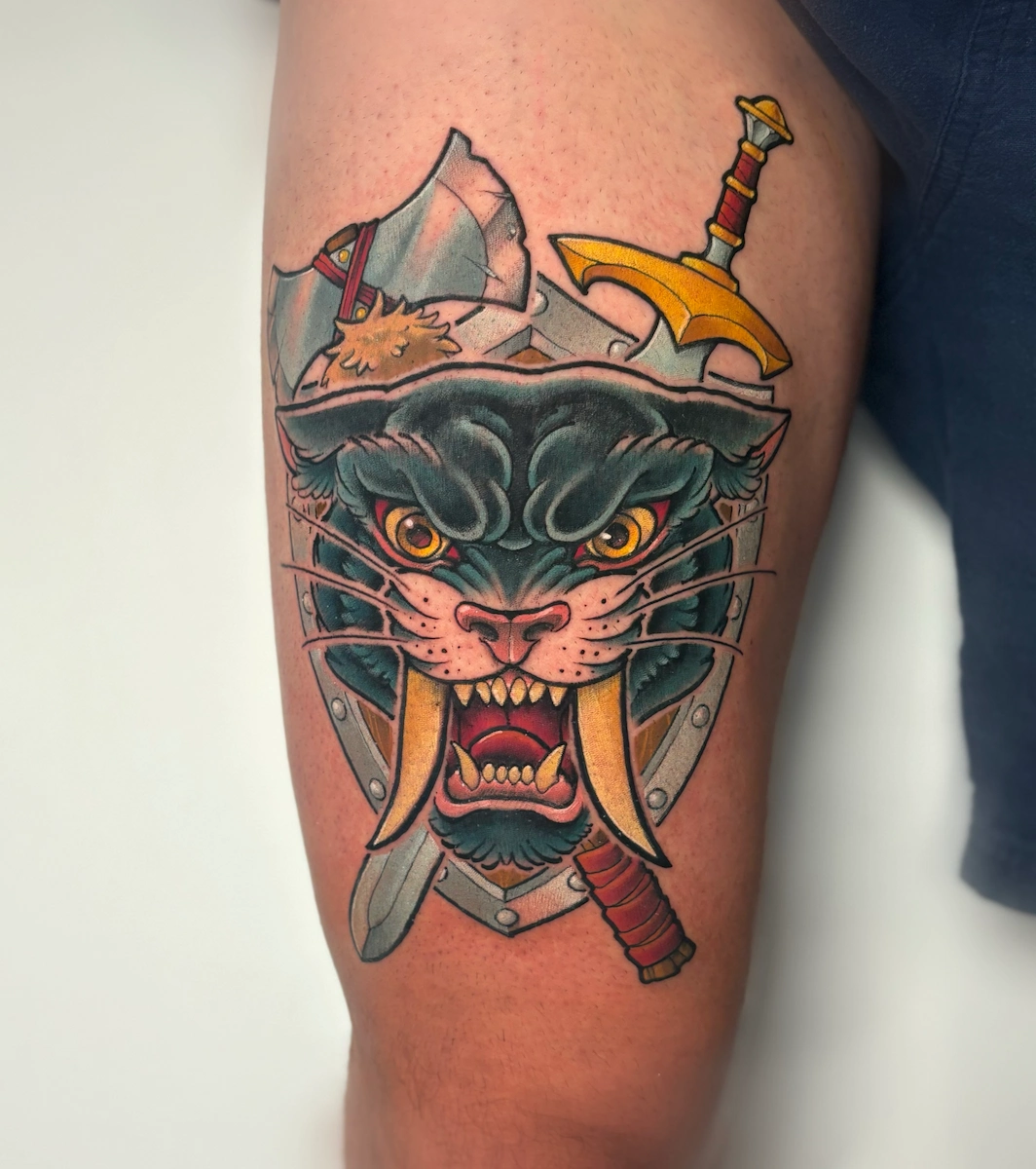 Tatouage noir représentant une tête de panthère sur des armoiries – Jake Tattoo Parlor à Belfort.