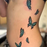 Tatouage de papillons bleus sur le flanc d’une femme – Jake Tattoo Parlor à Belfort.